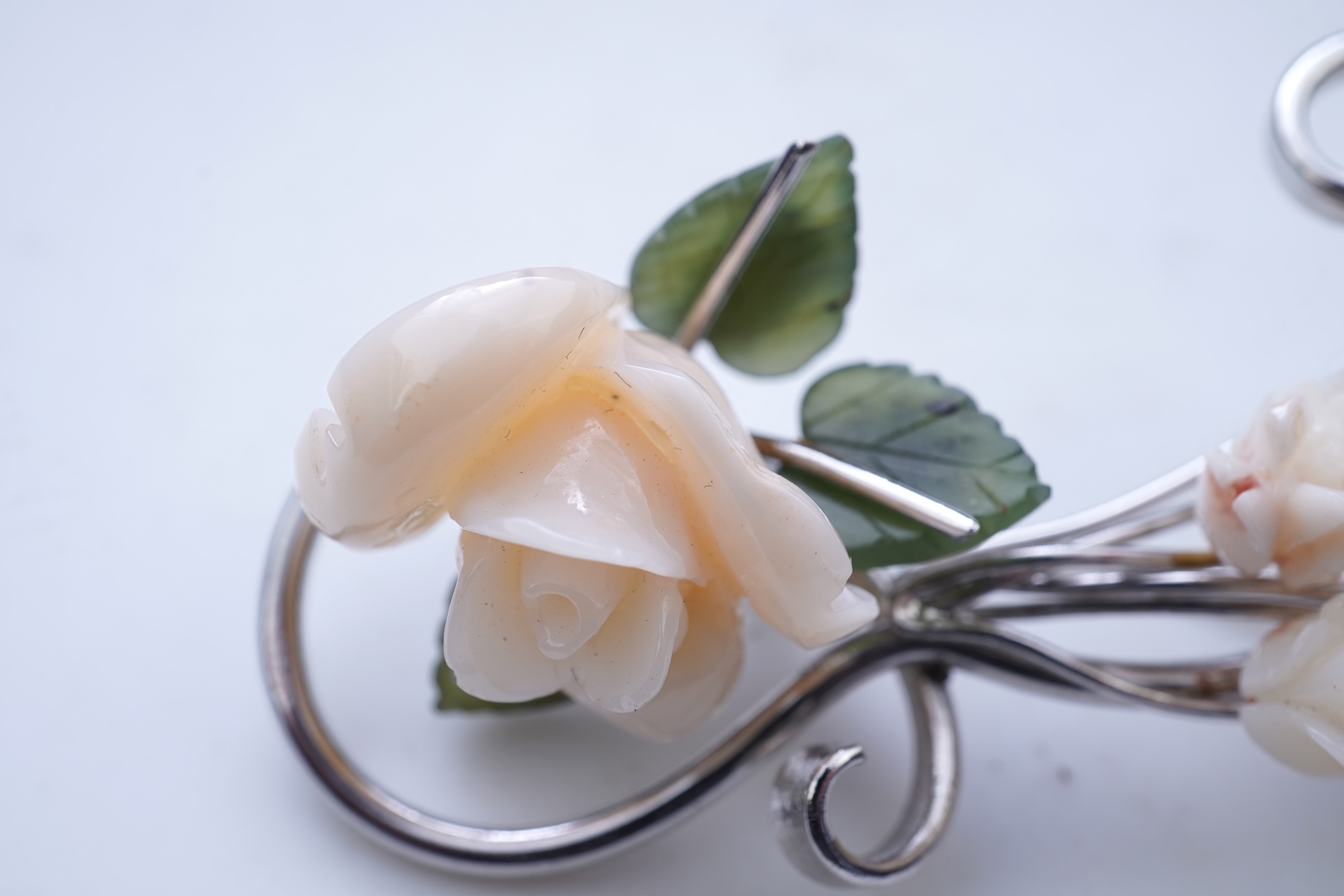 A white coral and nephrite brooch, designed as a spray of roses in carved white coral with nephrite leaves, on a scrolled white gold mount, length 5.5cm, stamped 14K, gross weight 11 grams